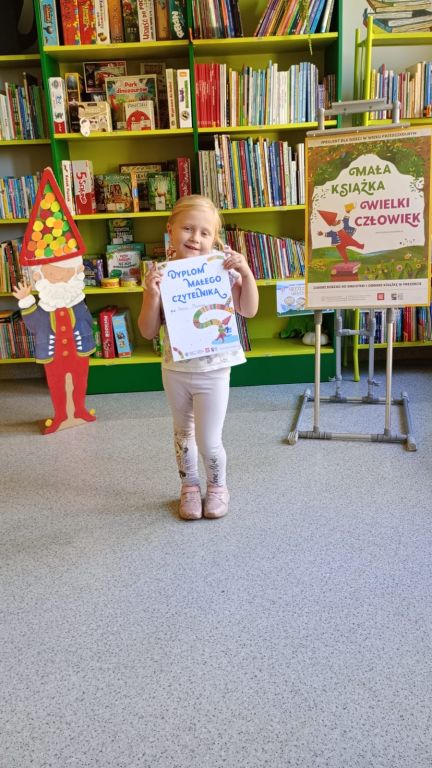 Dziewczynka trzyma w ręku dyplom Małego Czytelnika