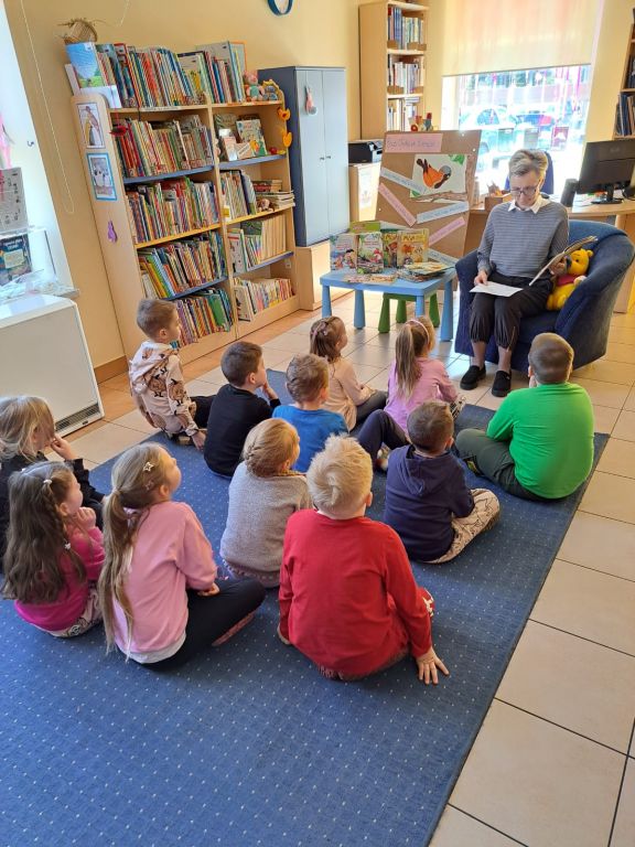 Bibliotekarz czyta dzieciom bajkę o Wróbelku, dzieci siedzą na dywanie