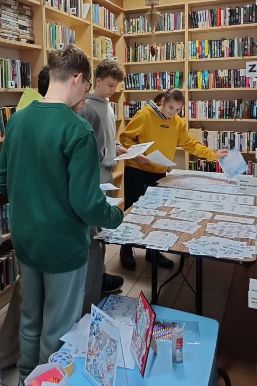 Czw&oacute;rka uczni&oacute;w stoi przy stole, na kt&oacute;rym rozłożone są materiały do scrapbookingu.