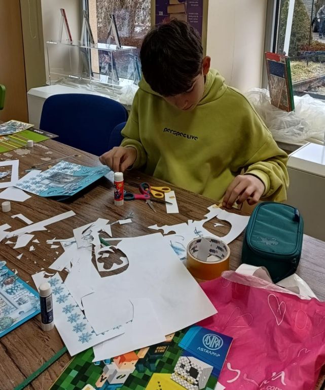 Chłopiec siedząc przy stole pochylony, pracuje na d swoją kartką.