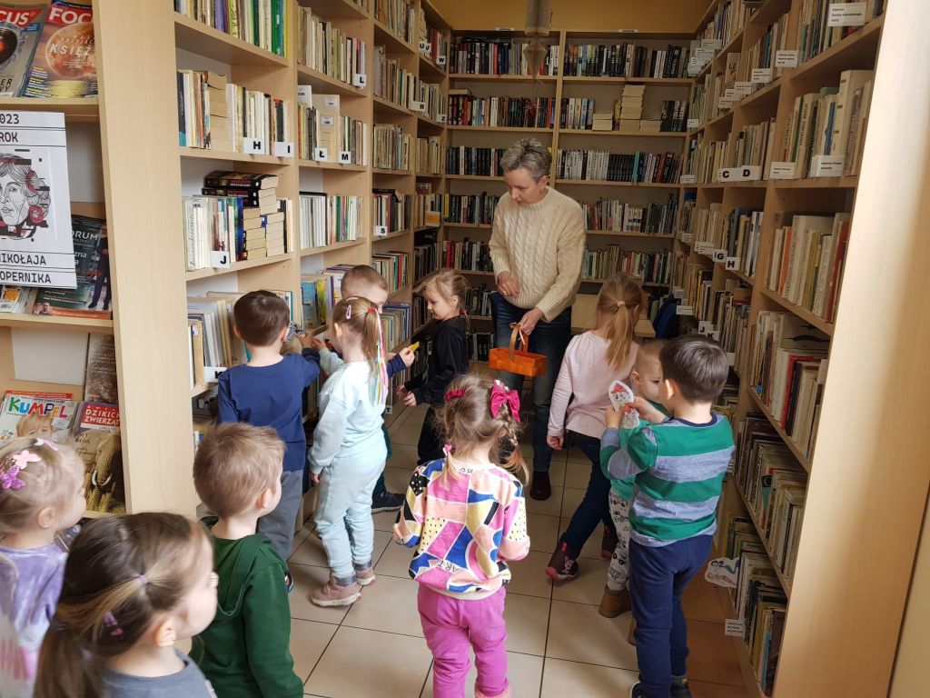 Dzieci szukają w bibliotece książek, w których mieszkają postacie bajkowe.