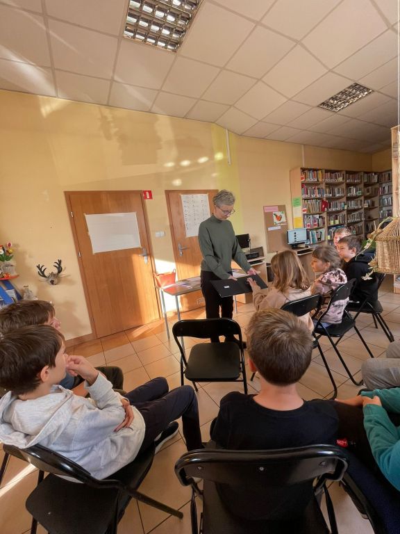 Dzieci siedzą na krzesłach i słuchają bibliotekarza