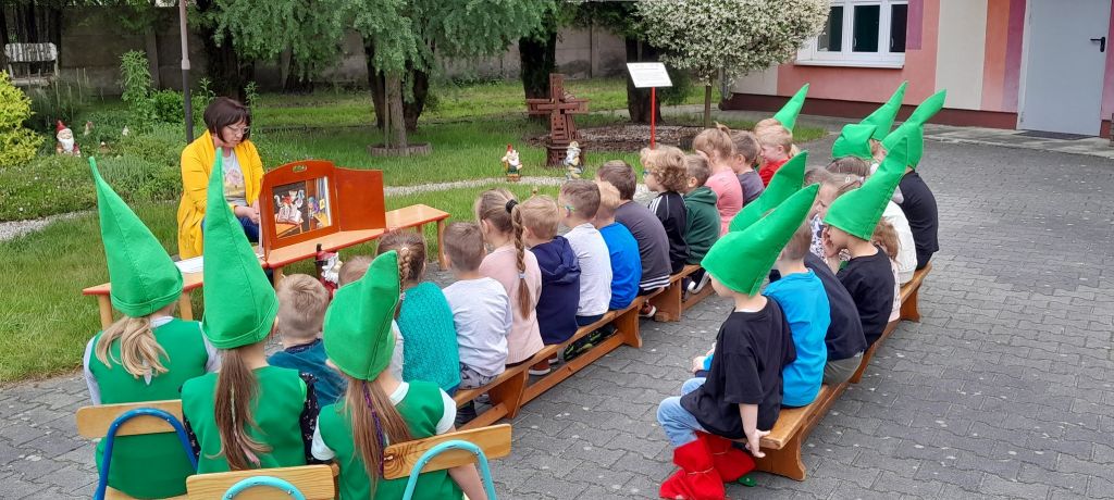 Dzieci słuchają bajki opowiedzianej przez bibliotekarza w formie teatrzyku kamishibai