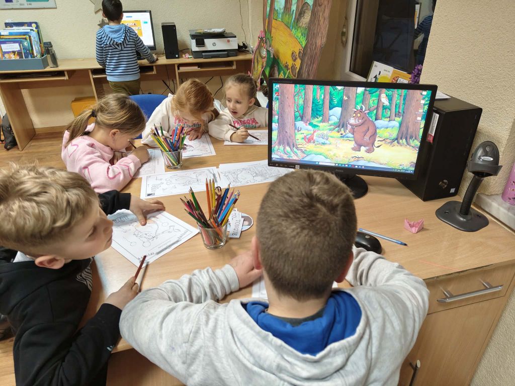 Grupa dzieci koloruje kolorowanki przy biurku.