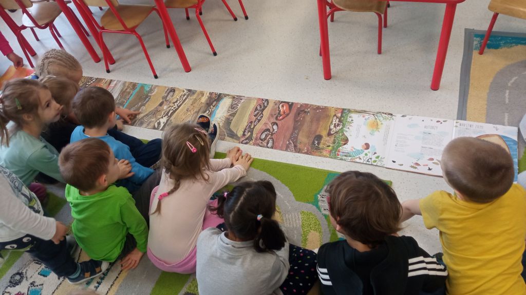 Dzieci oglądają rozwiniętą na ziemi bardzo długą książkę