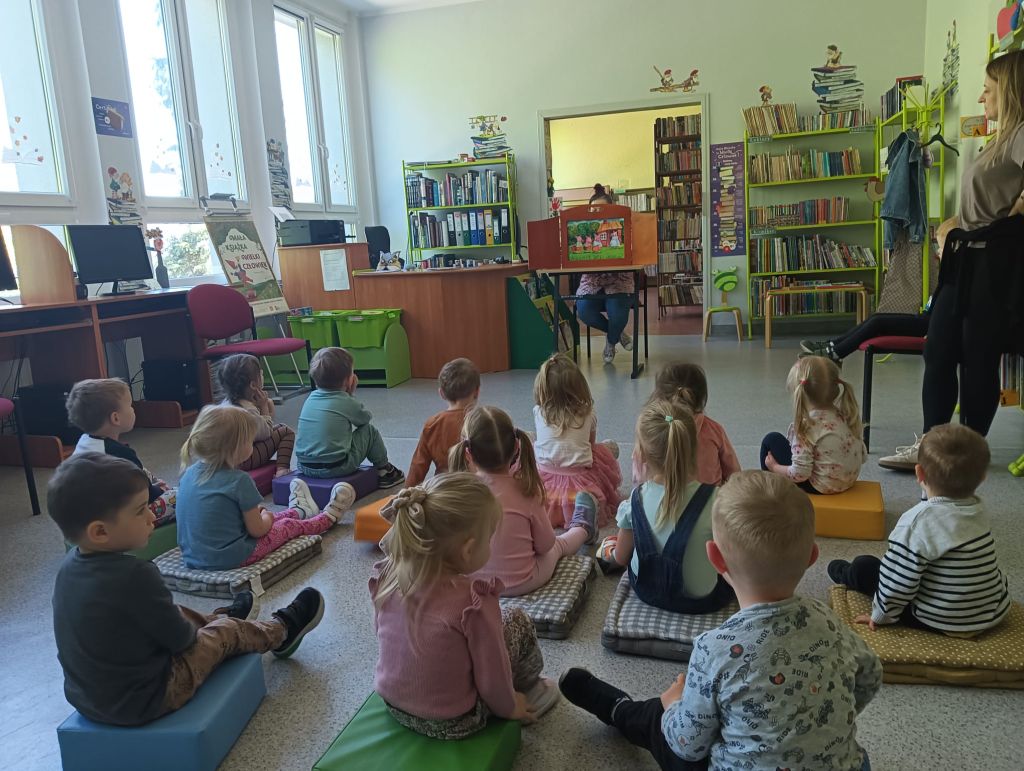 Bibliotekarz pokazuje obrazy w teatrzyku, dzieci siedzą i słuchają