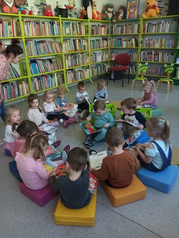 Dziecko w środku kółeczka przegląda książeczkę, wokół siedzą pozostałe dzieci