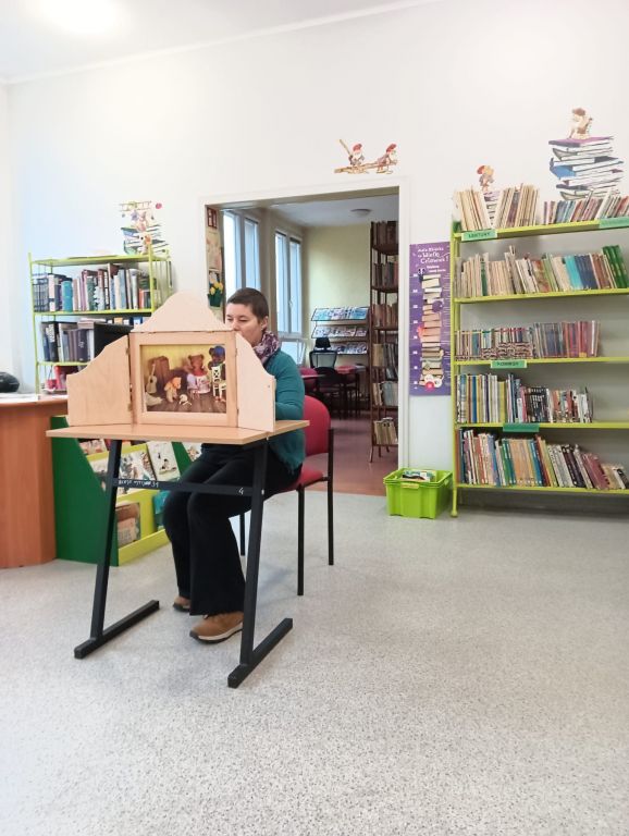 Bibliotekarz czyta dzieciom karty Złotowłosej w teatrzyku kamishibai