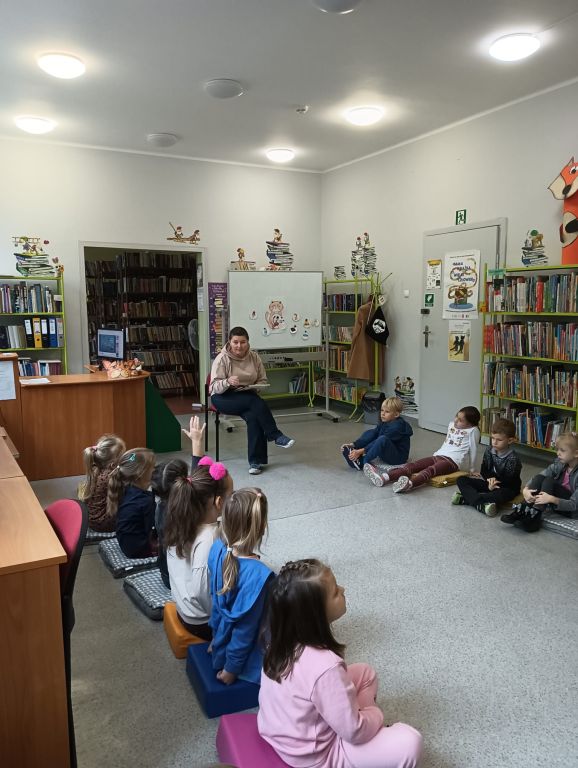 Dzieci siedzą w kole, na środku bibliotekarz