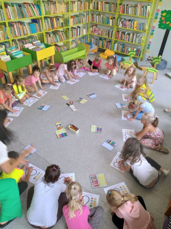 Dzieci siedzą w kole i wykonują zadnie na kartkach