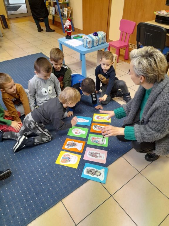 Bibliotekarka pokazuje dzieciom obrazki, aby wyjaśnić kto w innych krajach przynosi prezenty