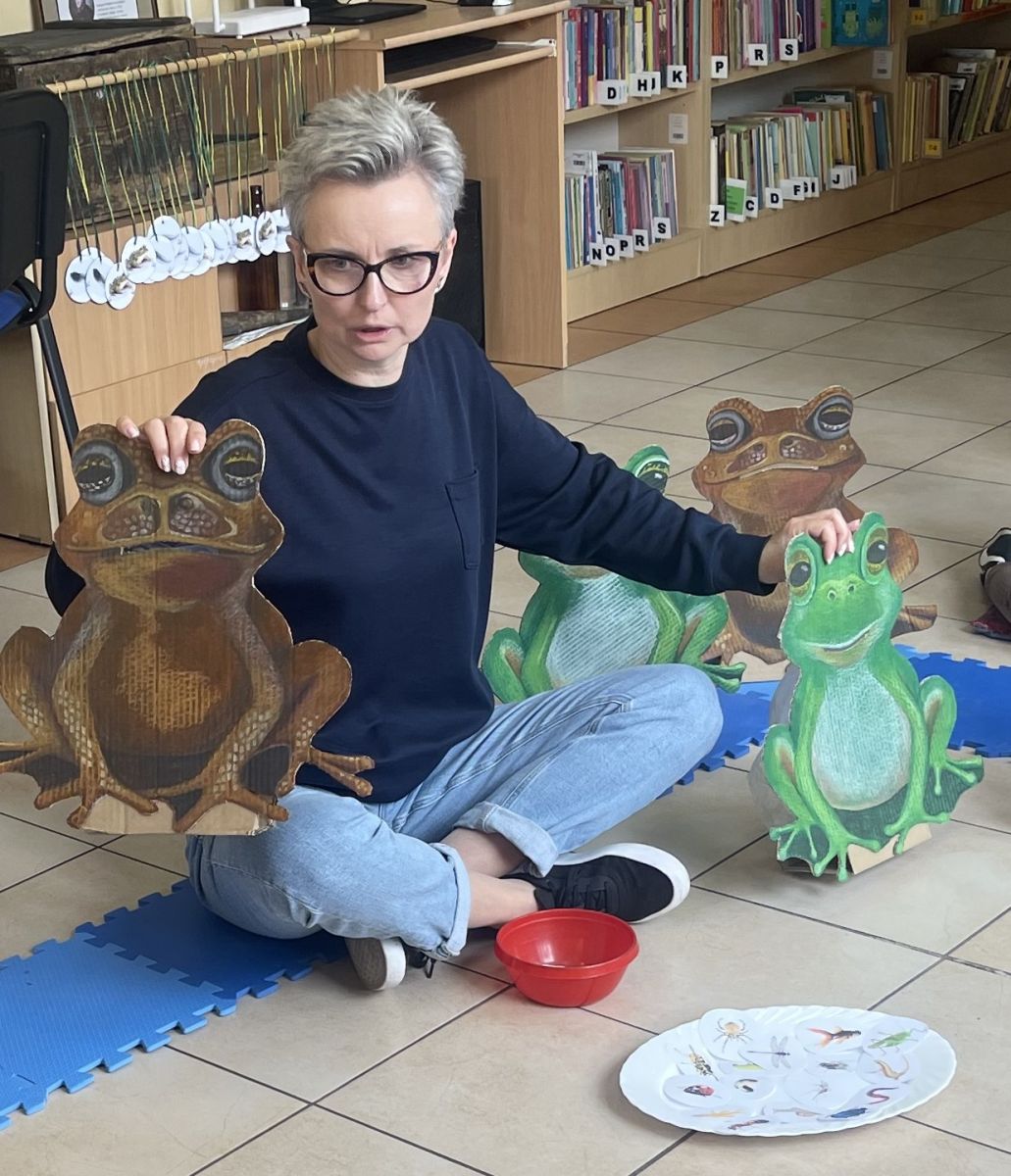 3-	Na podłodze siedzi bibliotekarka i trzyma w jednej ręce sylwetę żaby, w drugiej &ndash; ropuchy.