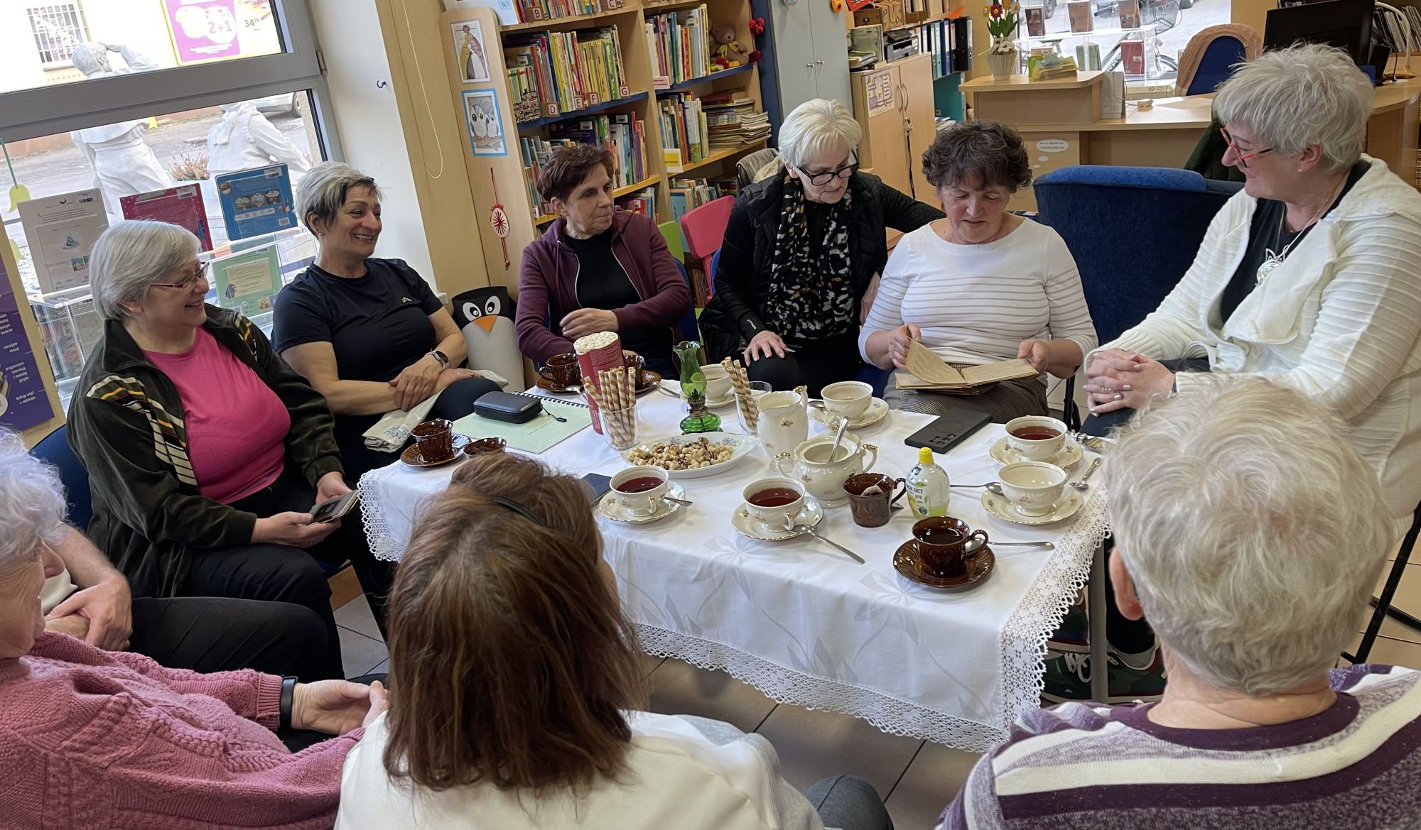 Grupa kobiet siedzących dookoła stolika, słuchają opowieści jednej z nich. 