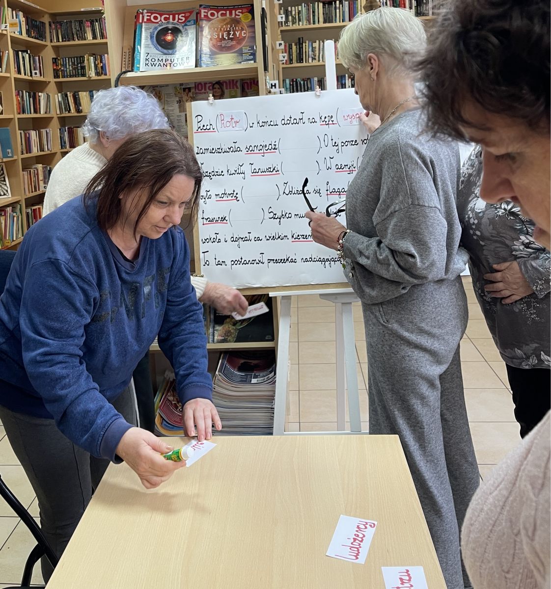 Pięć kobiet stojąc przed planszą analizuje słowa, rozsypane na stoliku.