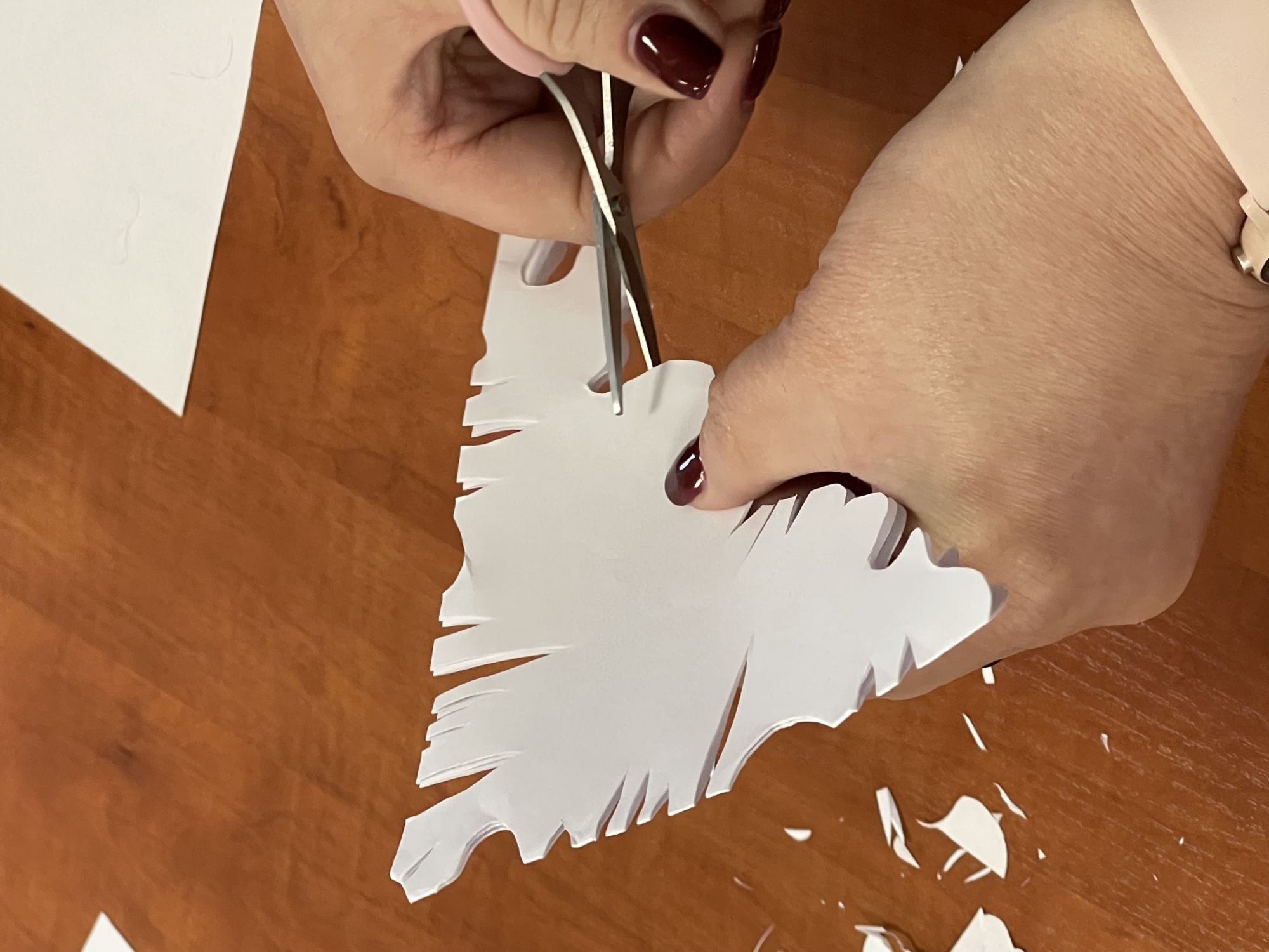 Zbliżenie na kobiece dłonie. W jednej jest złożony, biały papier, w drugiej maleńkie nożyczki, kt&oacute;rymi uczestniczka warsztat&oacute;w nacina papier.