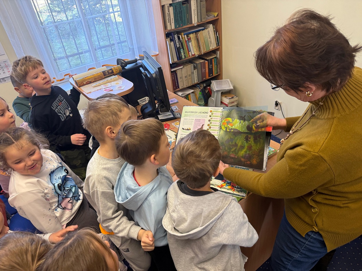 Pani bibliotekarka pokazuje dzieciom książkę z lupką.