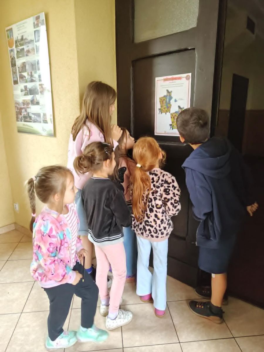 Grupa dzieci stoi i rozwiązuje kartę pracy przyklejoną do drzwi.