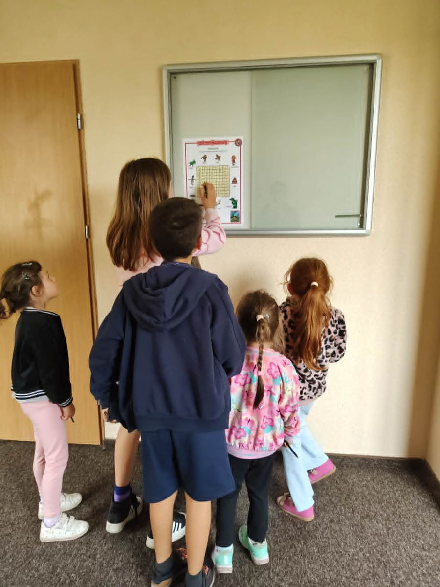  Grupa dzieci stoi i rozwiązuje kartę pracy przyklejoną do gabloty.