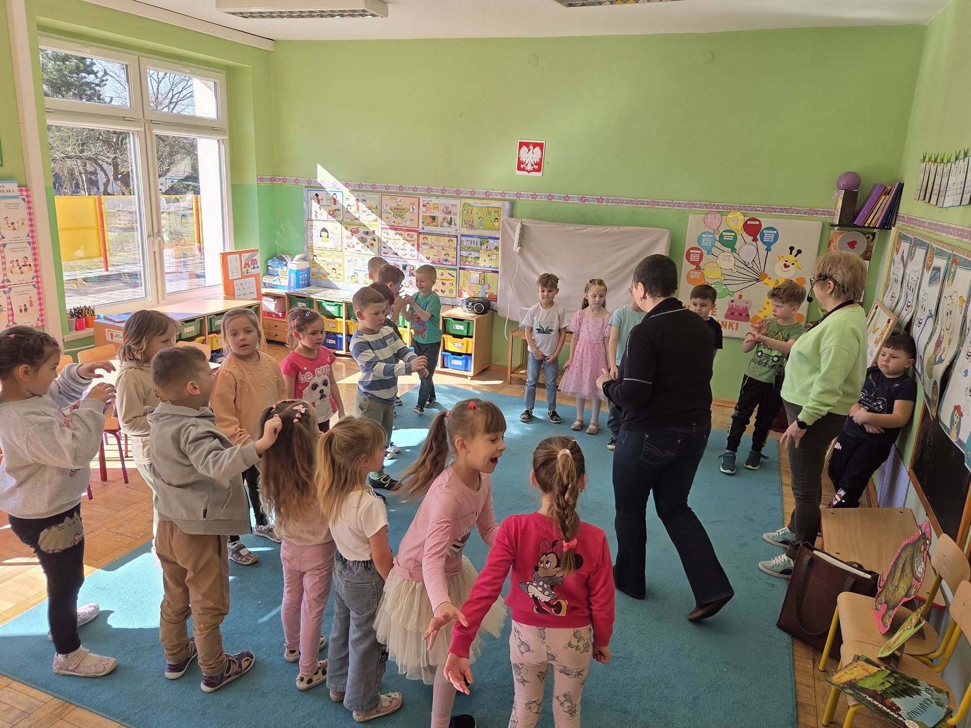 Dzieci wraz z panią bawią się w grupie w sali.