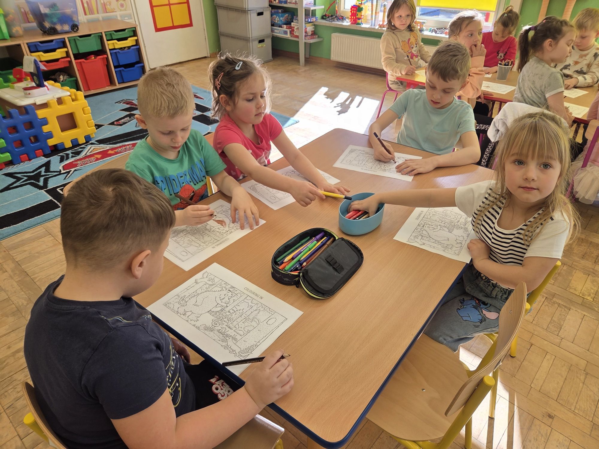Grupa dzieci siedzi przy stoliku kolorując kolorowankę Gruffalo.