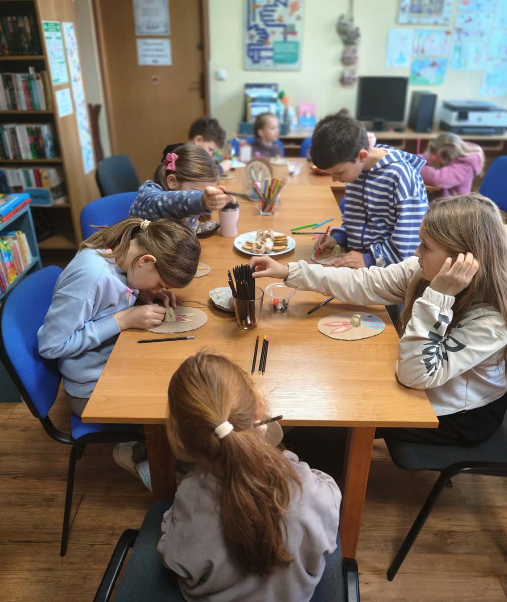 Dzieci siedzą przy stole i wykonują prace plastyczne.