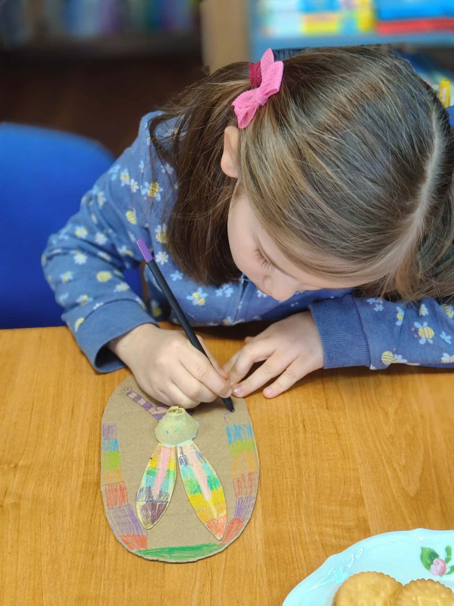 Dziewczynka siedzi przy stole i koloruje portret zająca wykonanego z tektury. 