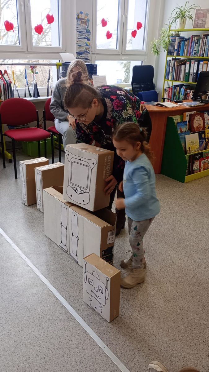 Pani wraz z dziewczynką buduje robota z kartonowych klock&oacute;w.