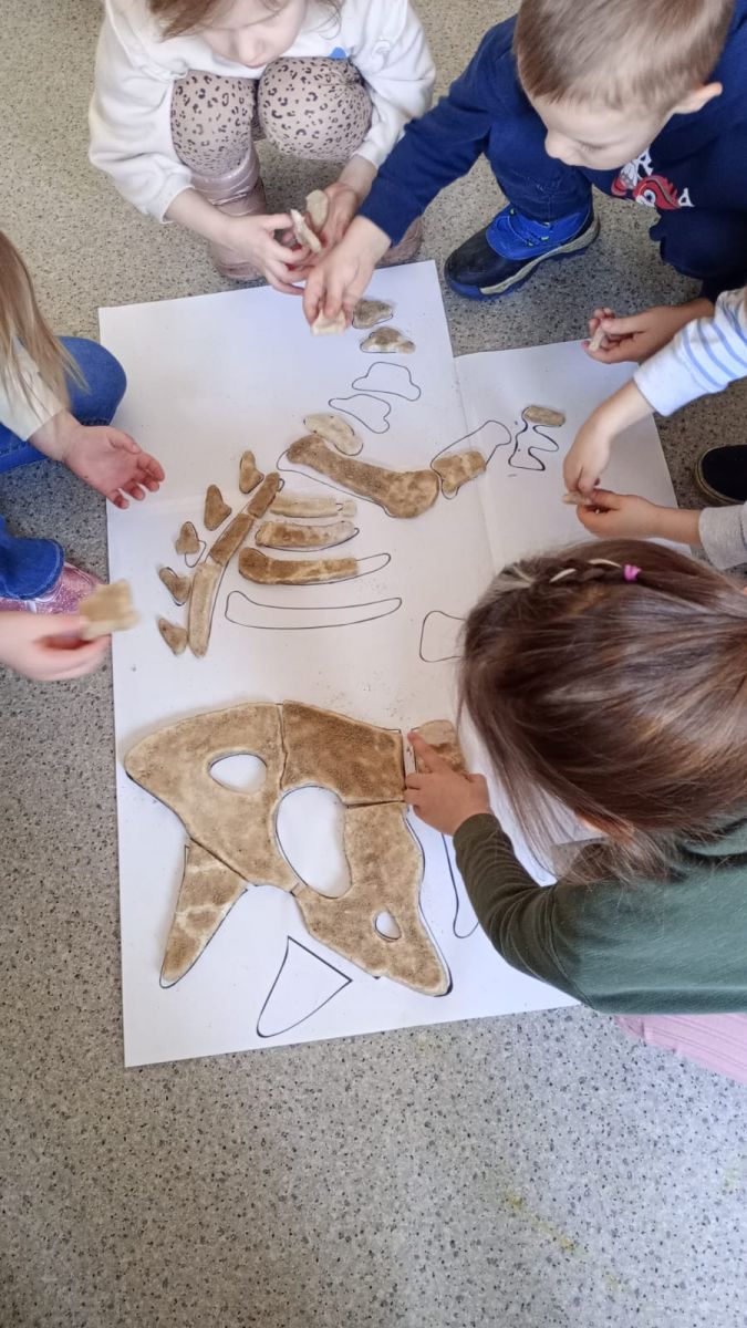 Dzieci układają szkielet dinozaura na planszy z wykopanych wcześniej kości wykonanych z masy solnej.