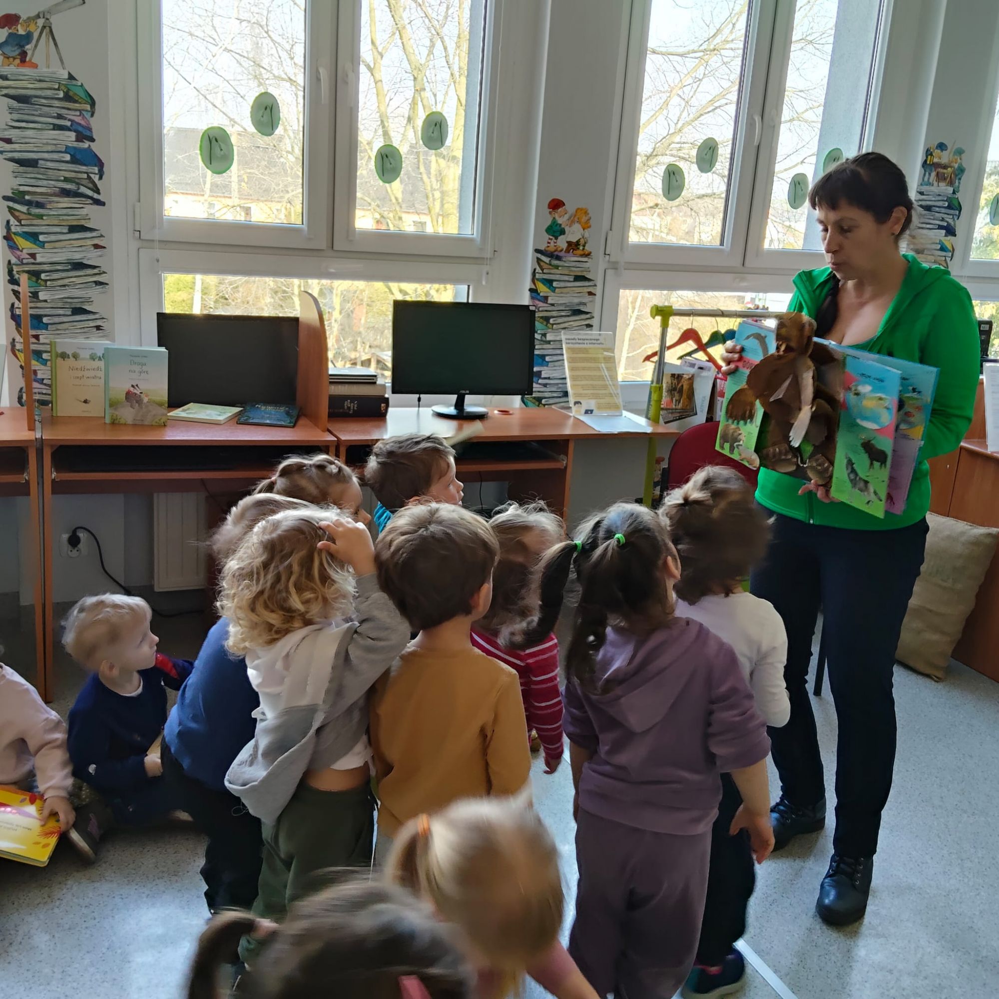 Pani pokazuje dzieciom książkę pop- up, z kt&oacute;rej wyłania się niedźwiedź.