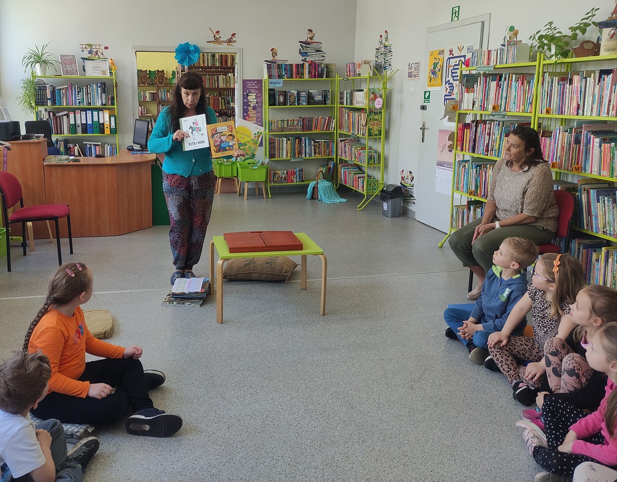 Pani Bibliotekarka pokazuje przedszkolakom wyprawkę czytelniczą.