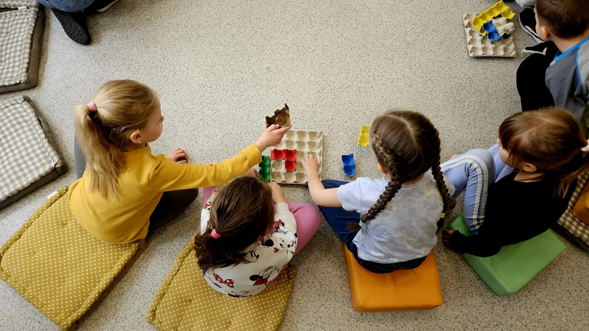 Dzieci w grupach rozwiązują zadanie - łamigł&oacute;wkę układając kolorowe wytłaczanki tak, aby zmieściły się one na jednej planszy.