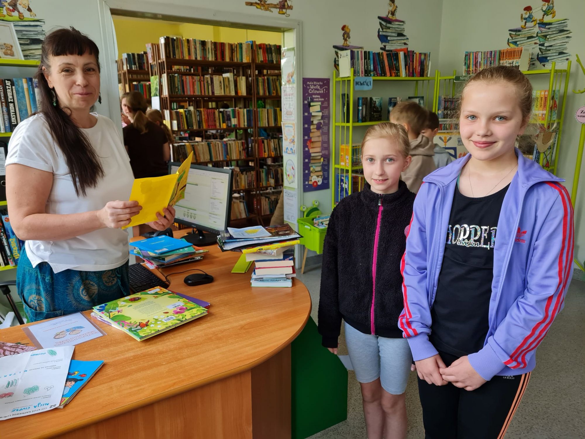 Dwie uczennice przekazują kartkę pani bibliotekarce z wyrazami uznania i podziękowania od wszystkich uczni&oacute;w.