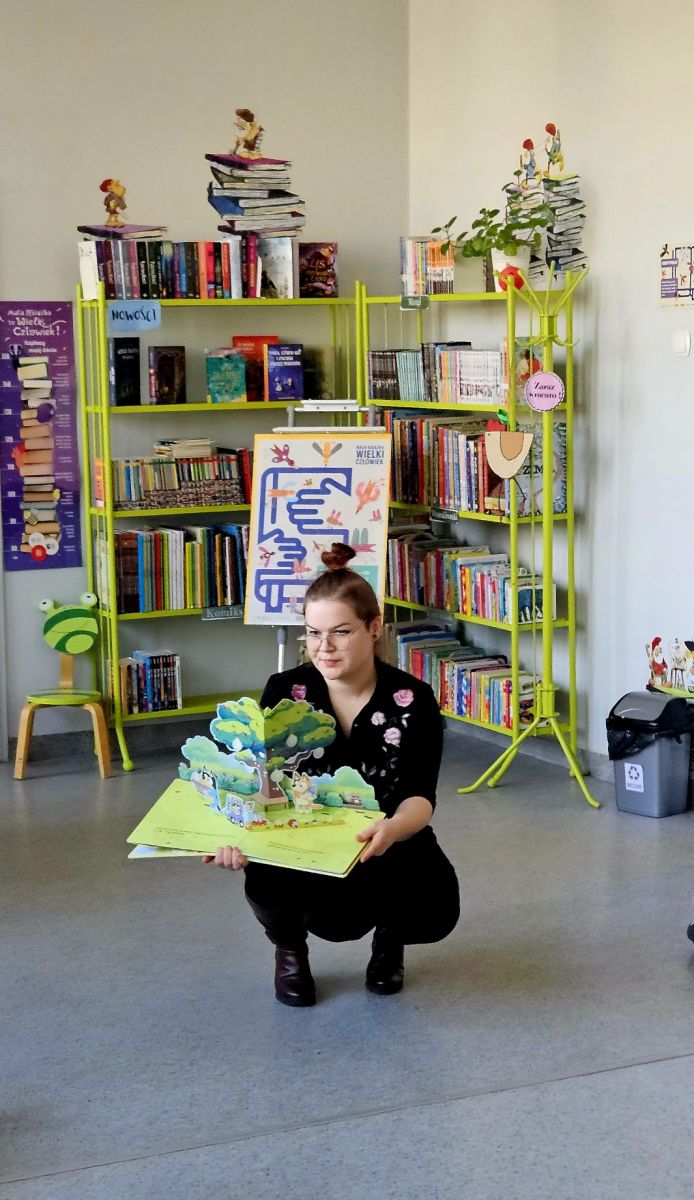 Młoda bibliotekarka pokazuje dzieciom książkę przestrzenną z serii Bluey