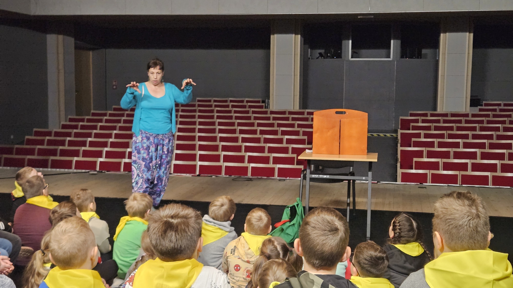 Bibliotekarka opowiada dzieciom zgromadzonym na scenie domu kultury historię teatrzyku kamishibai