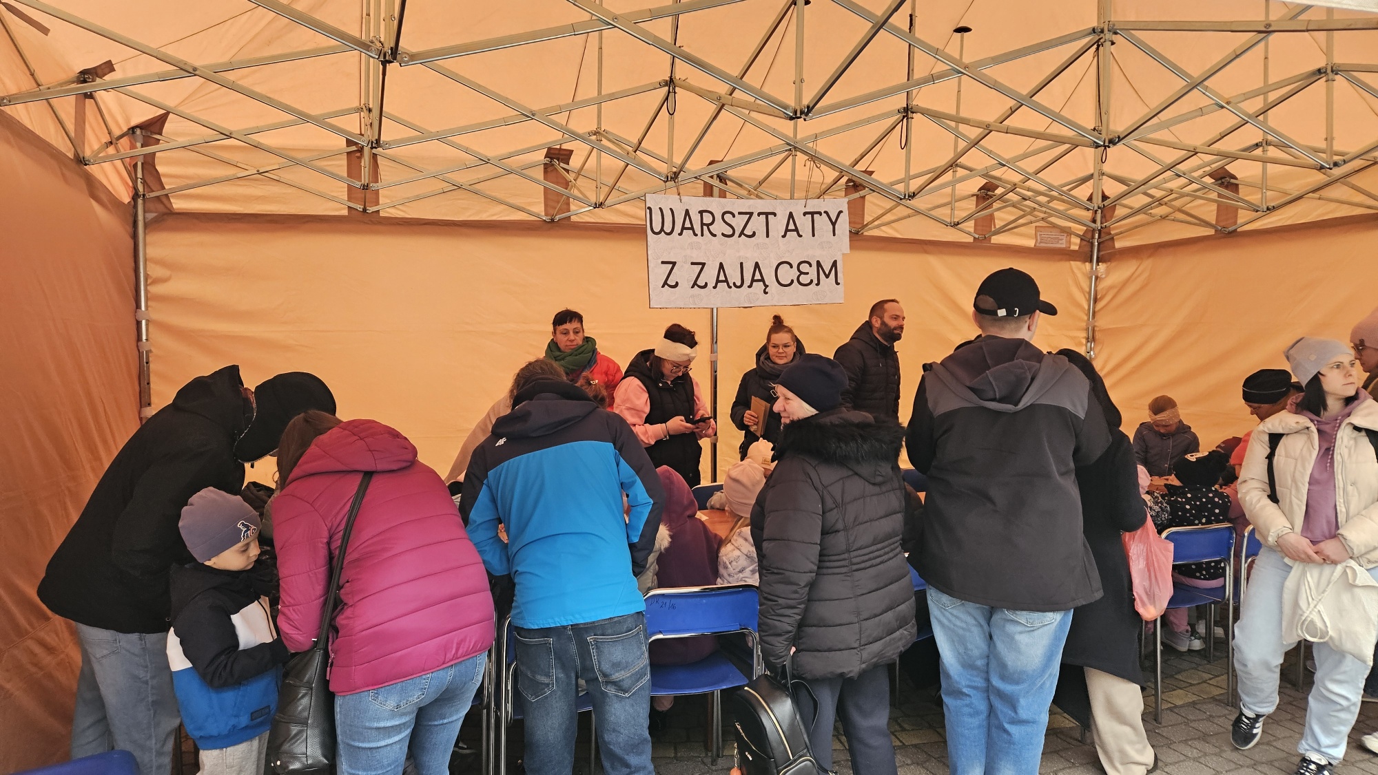 Dzieci siedzące przy stale wykonują prace plastyczne. Wok&oacute;ł rodzice