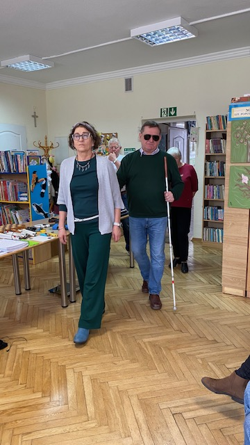Mężczyzna i kobieta prezentują prawidłowy spos&oacute;b prowadzenia osoby niewidomej